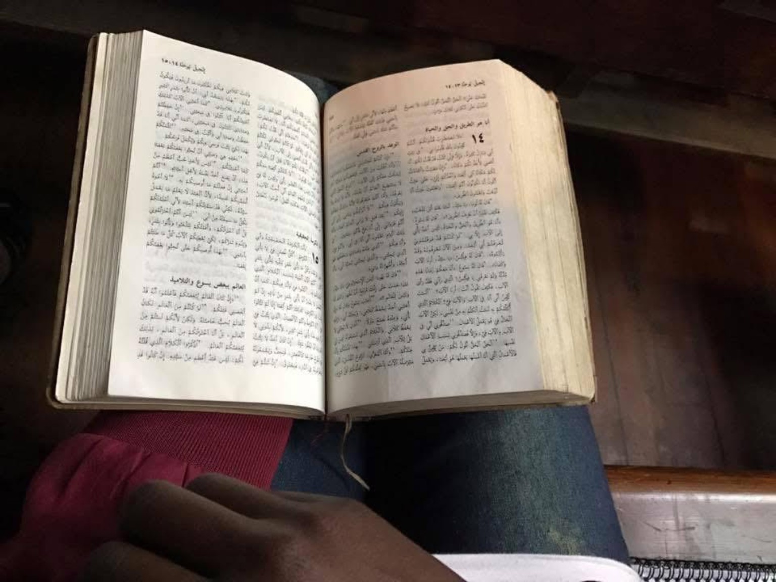An open Arabic Bible resting on a reader's lap